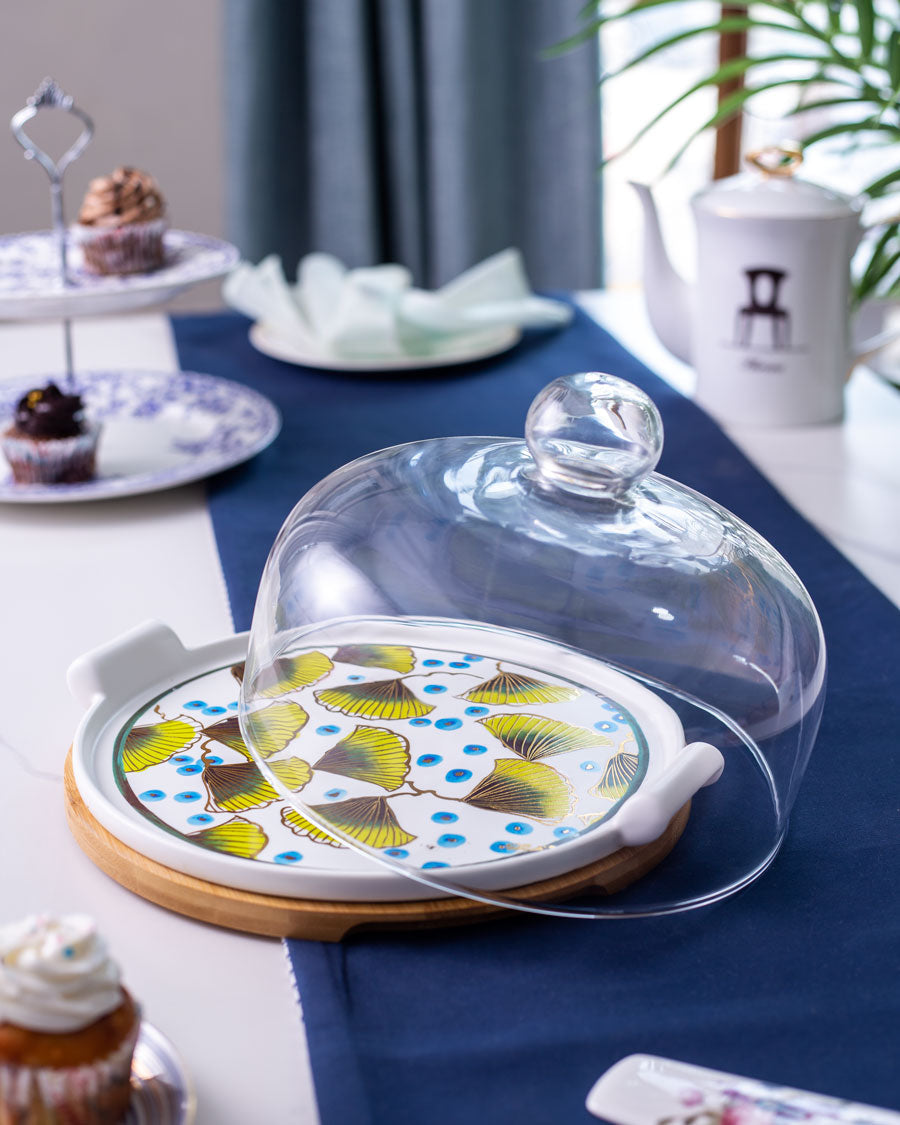 Elegant Ginkgo Cake Stand set on a blue tablecloth, with the dome lifted to display the colorful cake plate design.